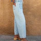 Person wearing light blue jeans and wooden sandals against a beige wall.