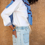 Person wearing a white shirt, blue jeans, and a blue scarf against a beige wall.