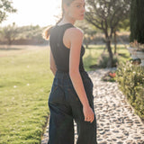 Woman in a black sleeveless top and dark blue jeans walking on a stone path in a garden.