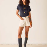 Woman wearing a navy t-shirt, white shorts, and dark rain boots against a plain background