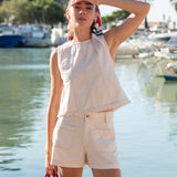 Woman in a light outfit standing by a waterfront with boats in the background