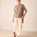 Woman in a beige cashmere knit short-sleeve crewneck top and cream linen pants.