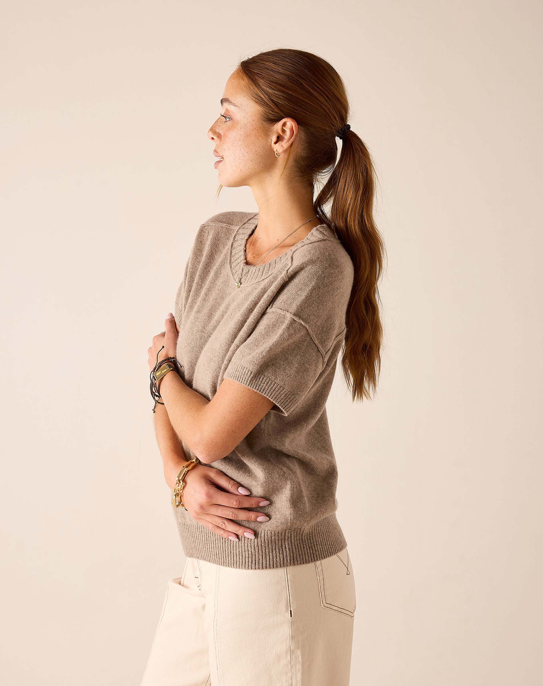 Woman in a beige cashmere crewneck short-sleeve knit top and cream-colored pants.
