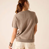 A person from behind wearing a beige cashmere crewneck short-sleeve knit top and off-white pants.