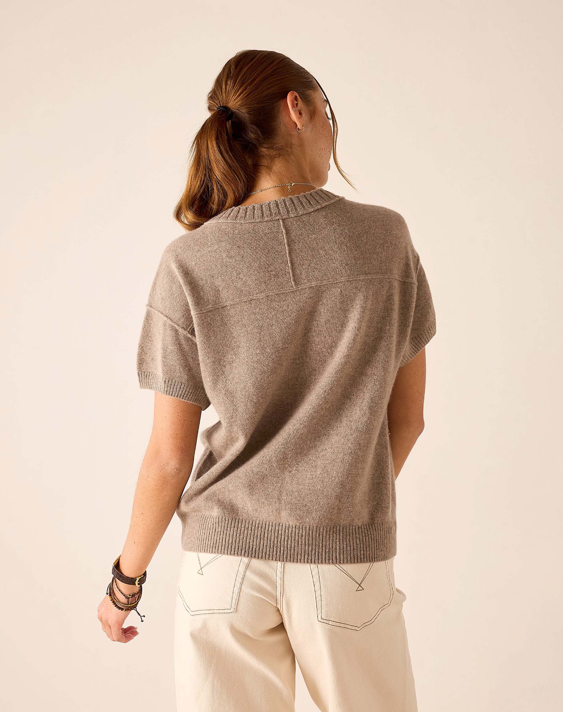 A person from behind wearing a beige cashmere crewneck short-sleeve knit top and off-white pants.