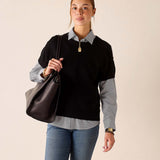 Woman in a black cashmere crewneck sweater over a grey button-down shirt and blue jeans.