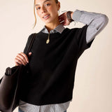 Woman in a black cashmere crewneck sweater over a striped button-up shirt and blue jeans.