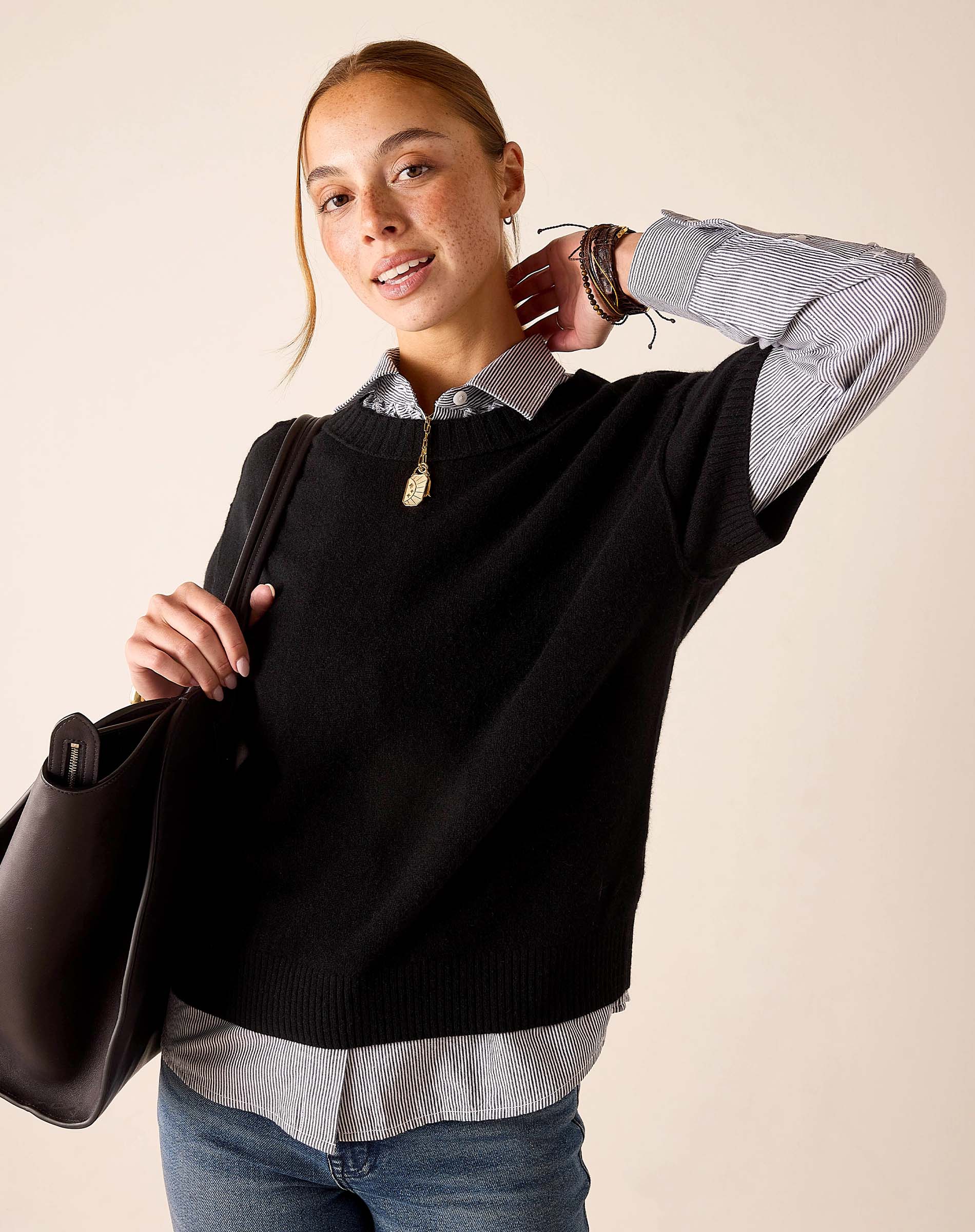 Woman in a black cashmere crewneck sweater over a striped button-up shirt and blue jeans.