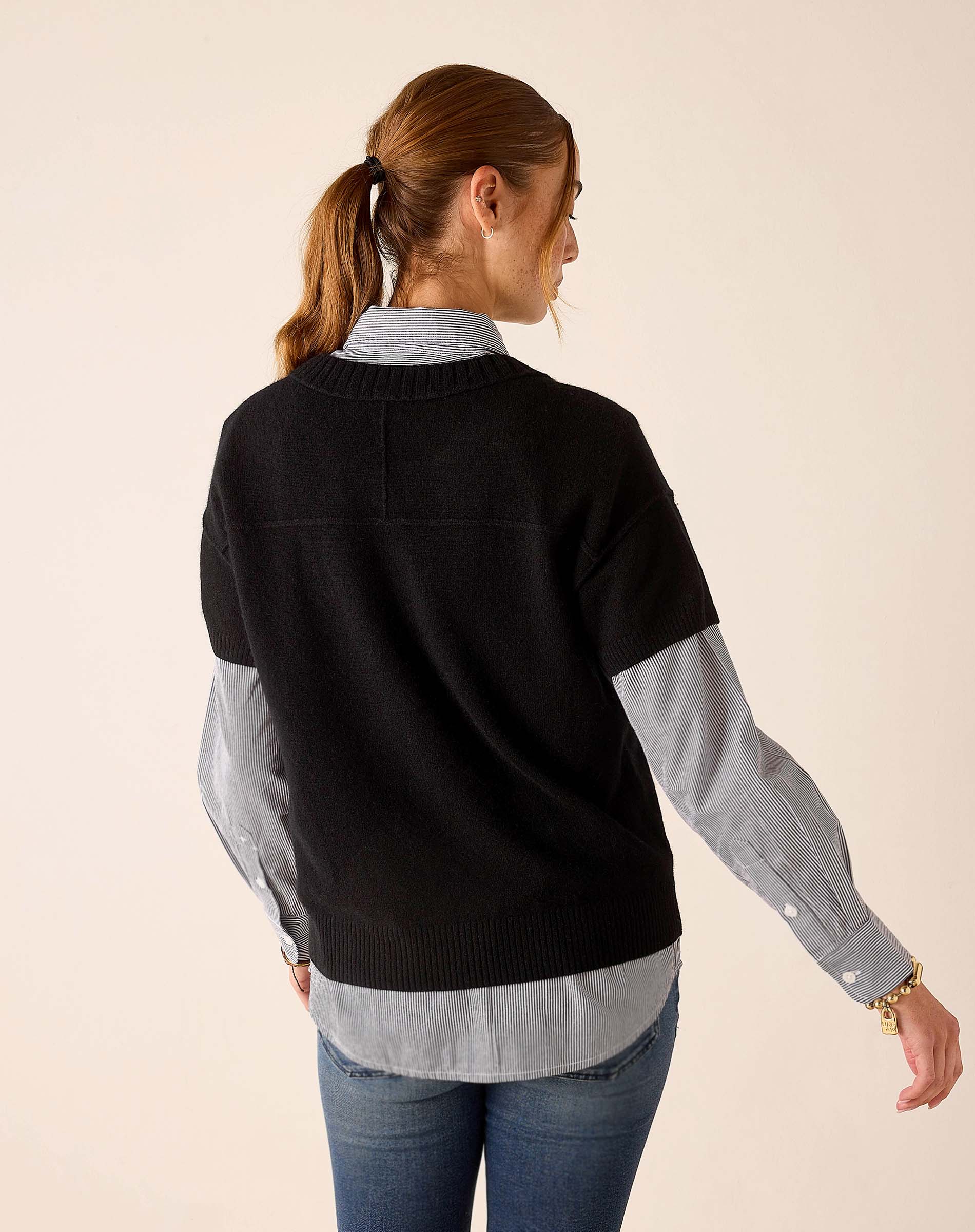 Model from behind wearing a black cashmere crewneck sweater over a light blue striped button-down shirt and jeans.