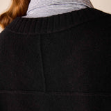 A woman in a black cashmere crewneck sweater over a blue and white striped shirt.