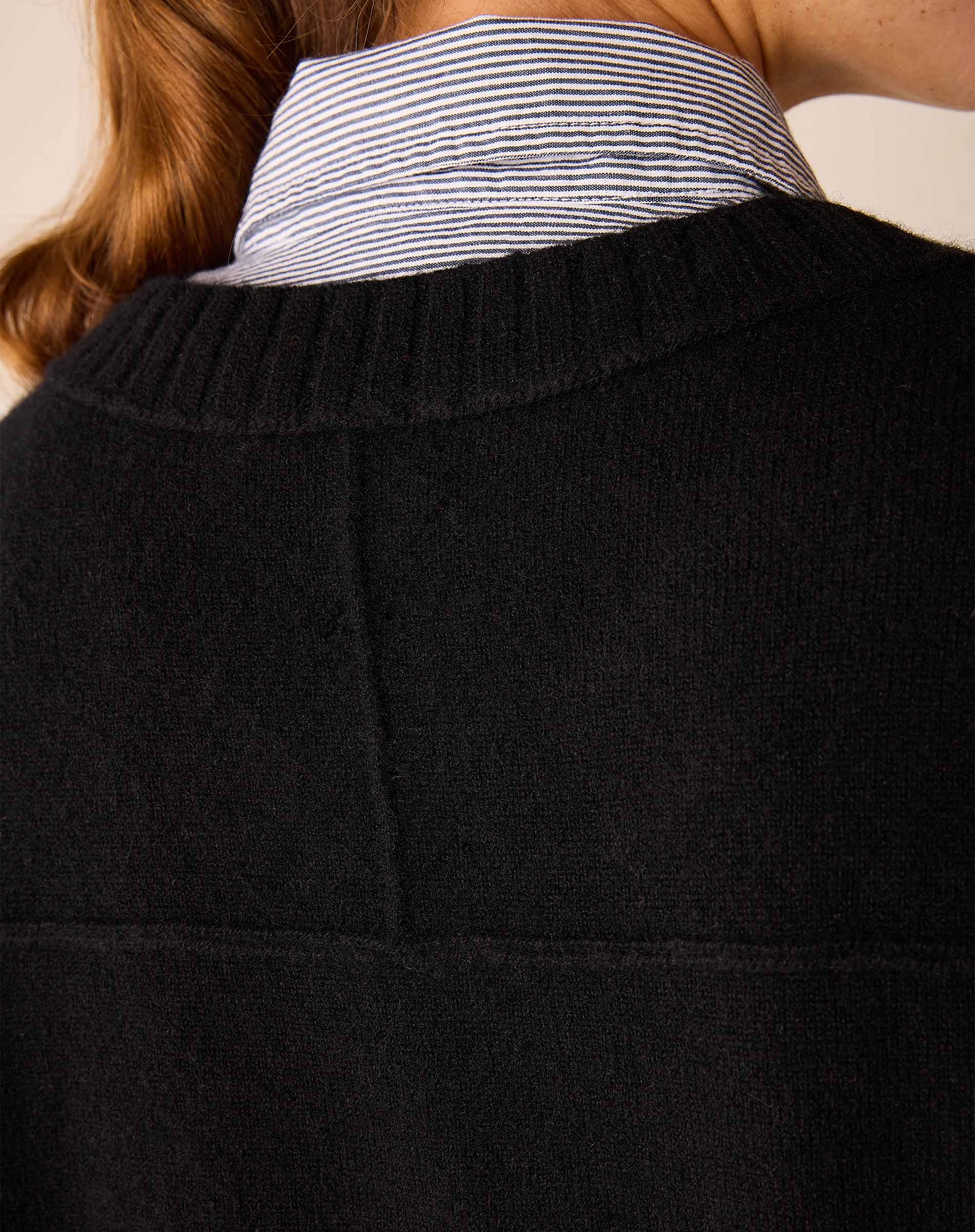 A woman in a black cashmere crewneck sweater over a blue and white striped shirt.