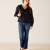 Woman wearing a black sweater and blue jeans against a plain background