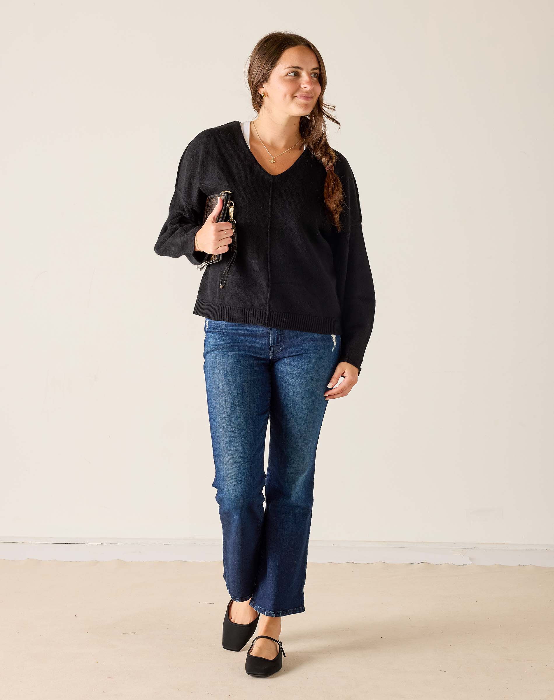 Woman wearing a black sweater and blue jeans against a plain background