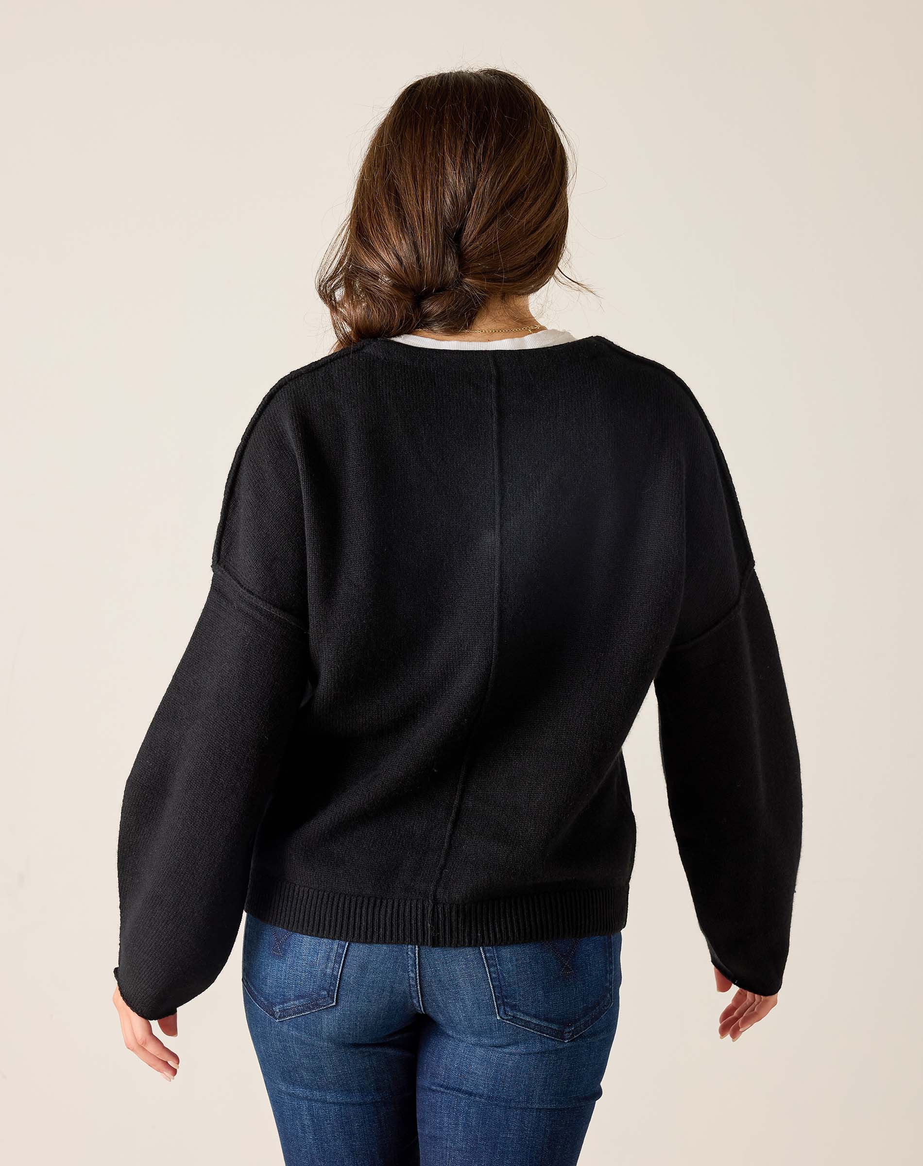 Person wearing a black sweater and blue jeans on a plain background