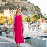 Woman in a pink dress standing on a dock with boats and a scenic background