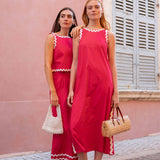 Two women in red dresses standing against a pink wall.