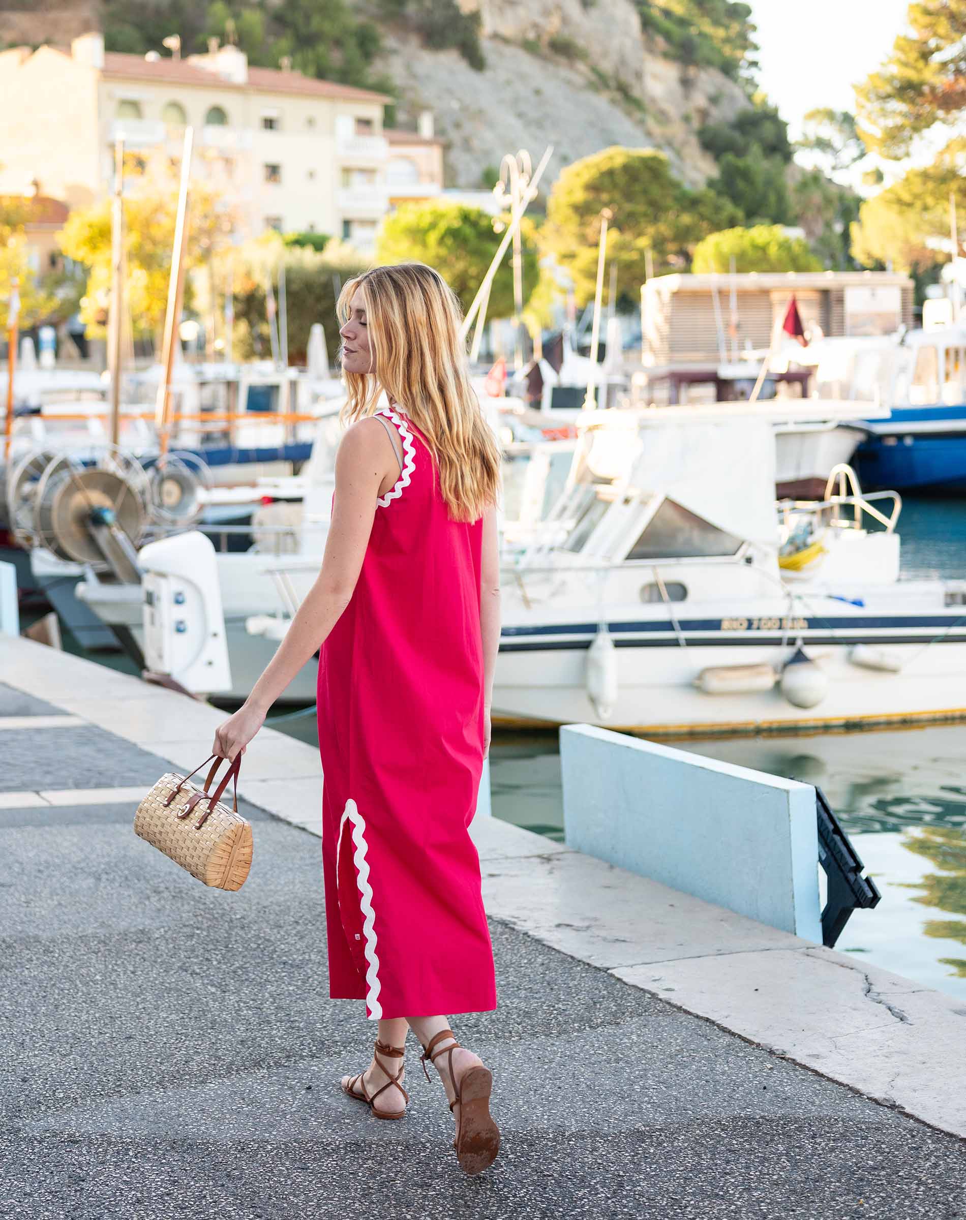 Woman in a pink dress walking along a harbor with boats in the background
