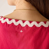 Close-up of a person wearing a red top with white lace trim and a gold necklace.
