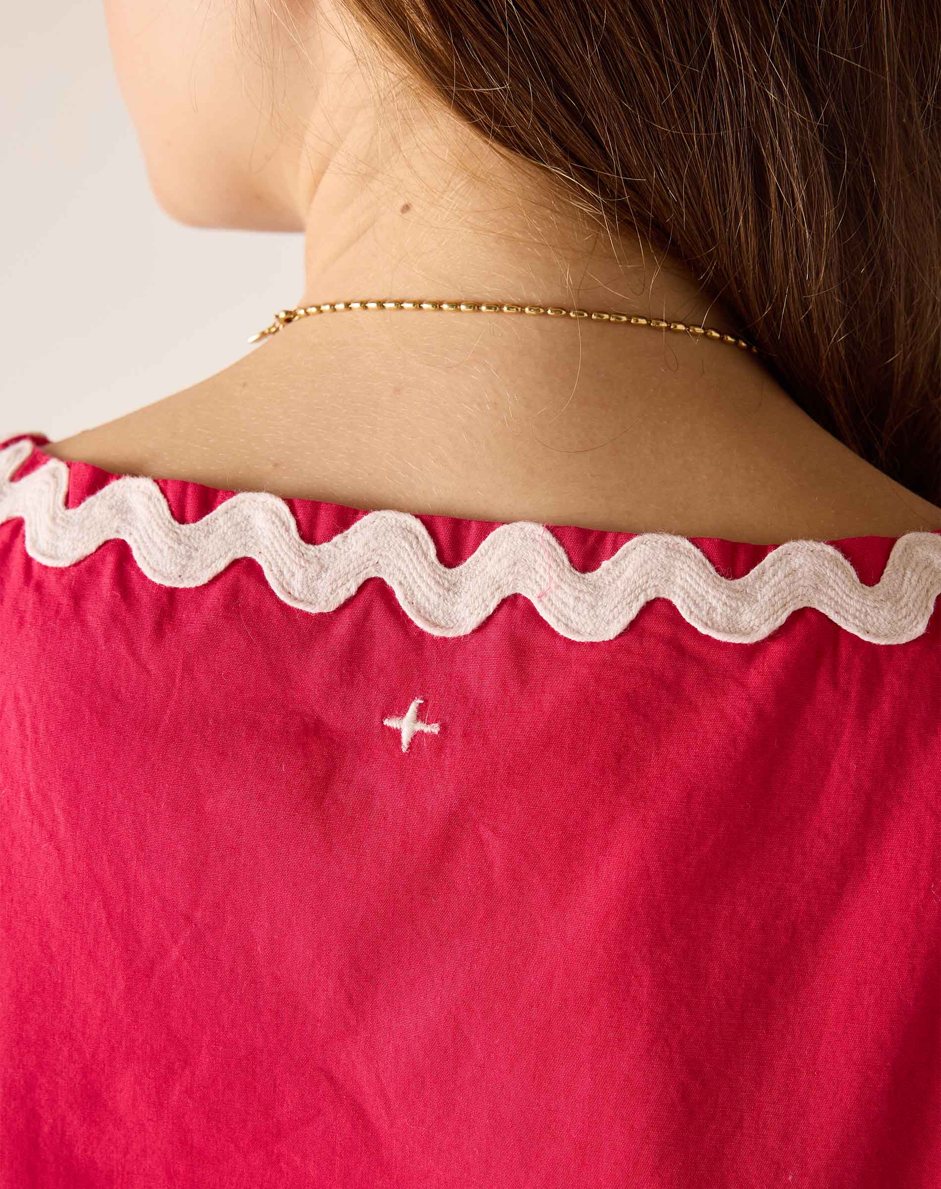 Close-up of a person wearing a red top with white lace trim and a gold necklace.