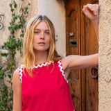 Woman wearing a red top with white trim standing in front of a wooden door.