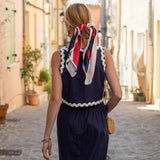 Woman in a navy dress with a colorful scarf walking down a sunlit street.