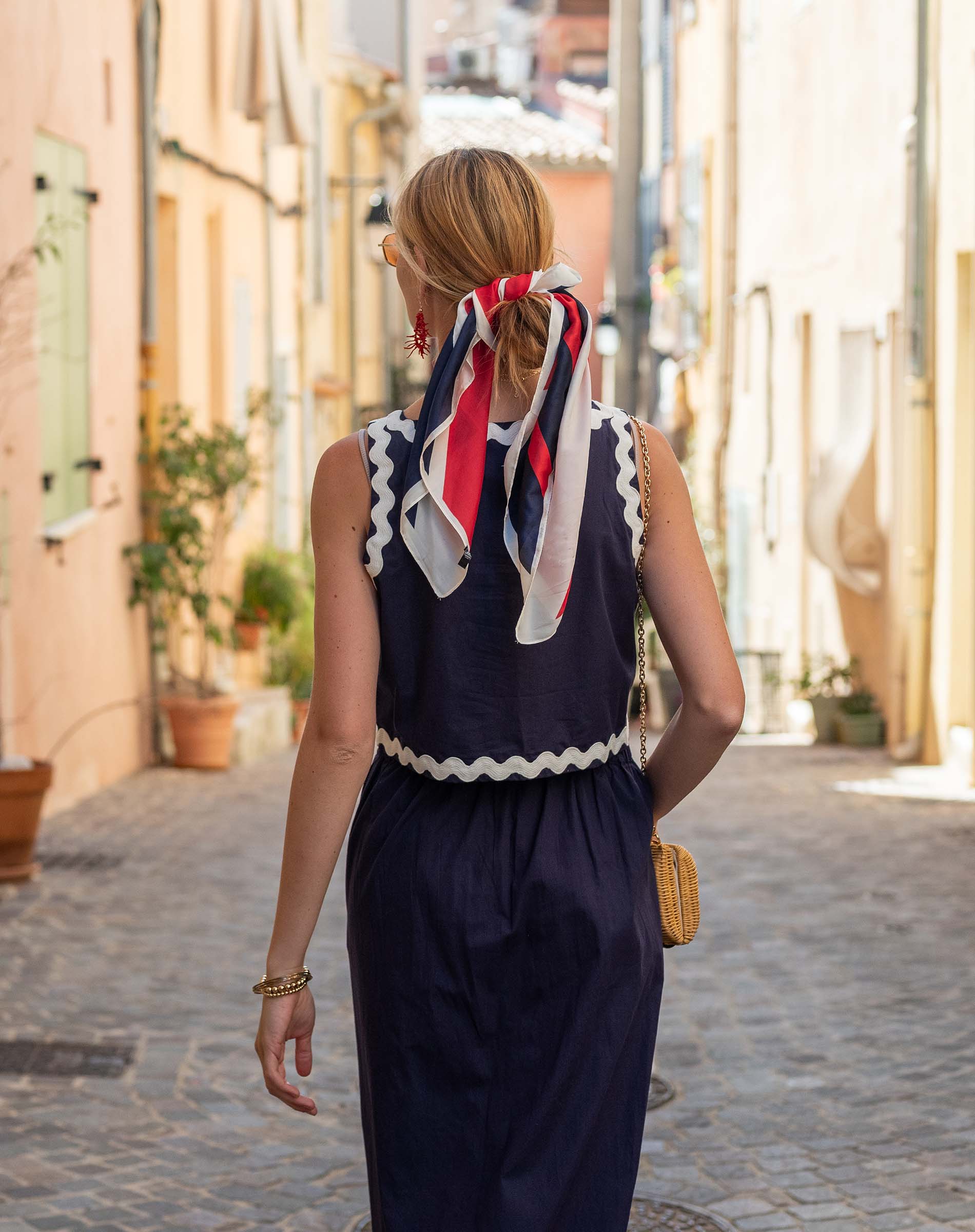 Woman in a navy dress with a colorful scarf walking down a sunlit street.