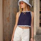 Woman wearing a navy top with white trim and white shorts, standing against a wooden wall.