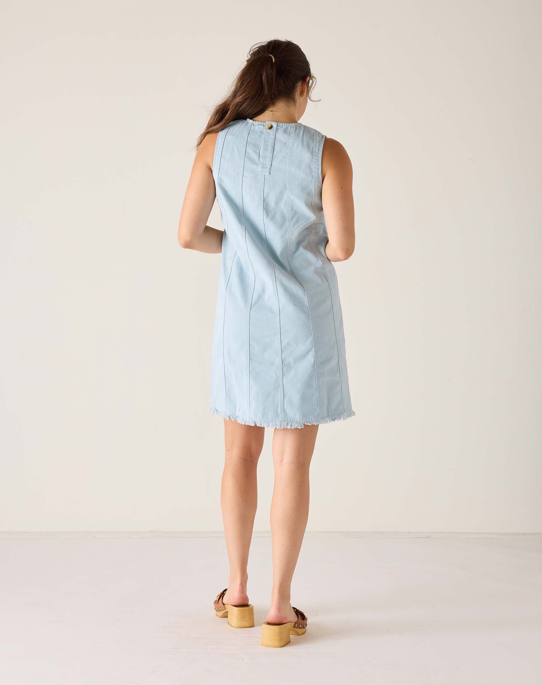 Back view of the light blue twill dress with a sleeveless design and raw hem.