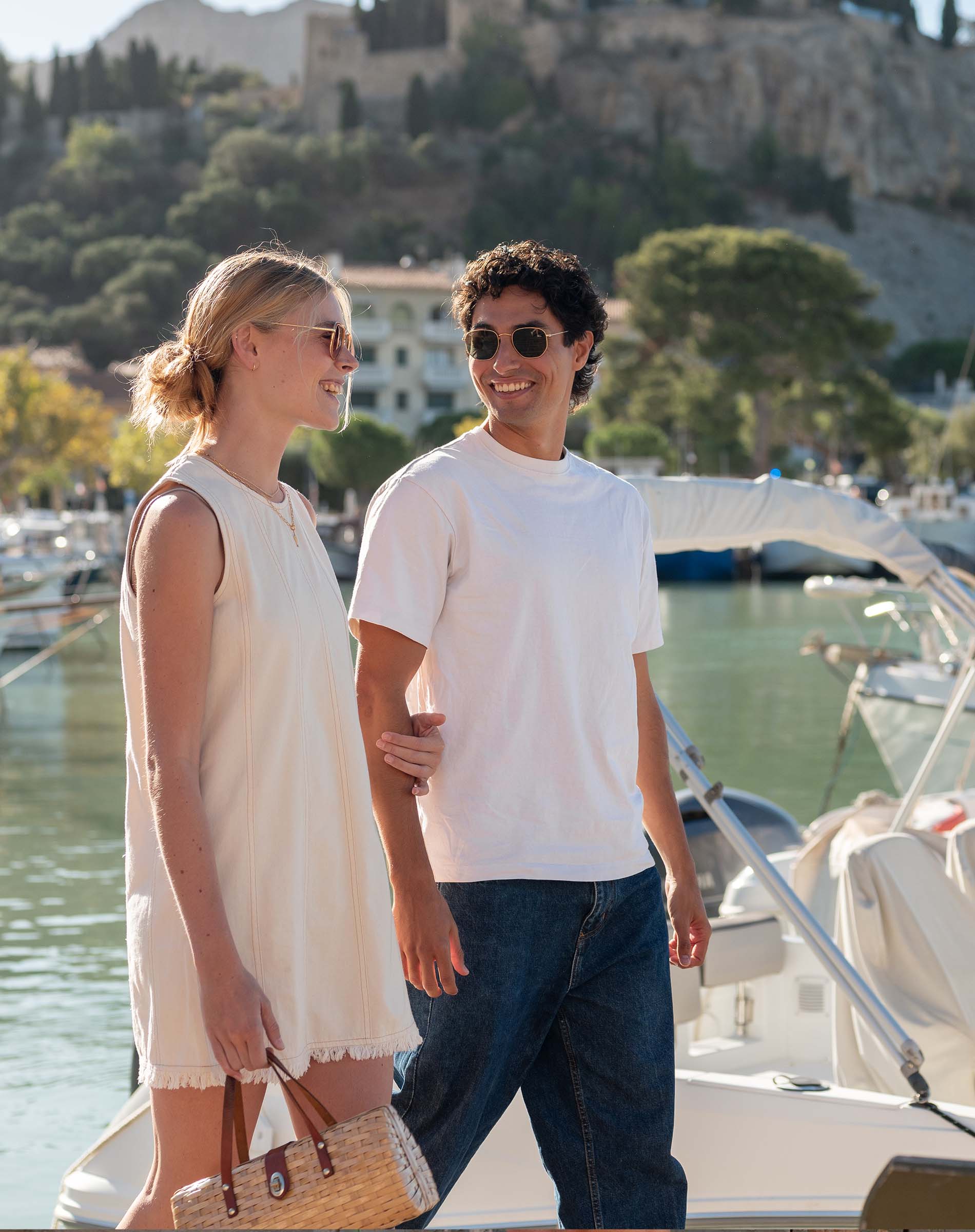 Two people standing on a dock with boats and a scenic background