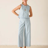 Woman wearing a light blue sleeveless top and wide-leg pants against a beige background