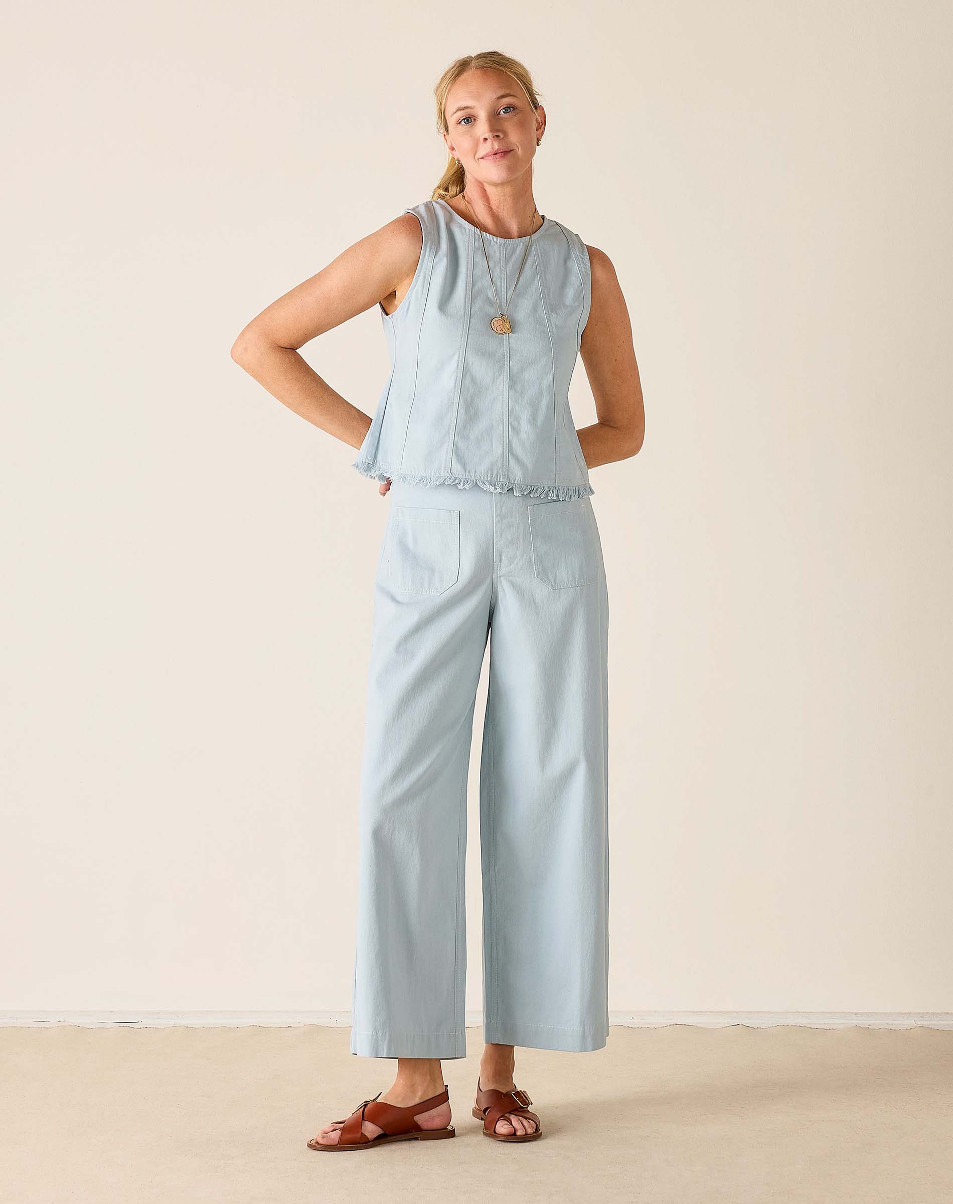 Woman wearing a light blue sleeveless top and wide-leg pants against a beige background