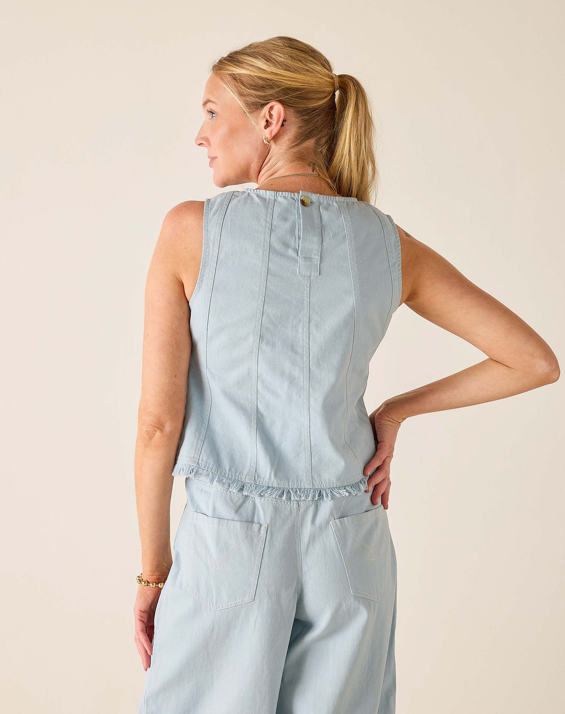 Woman wearing a light blue sleeveless top and pants against a beige background