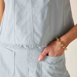 Light blue sleeveless top worn by a person with a gold bracelet on a neutral background