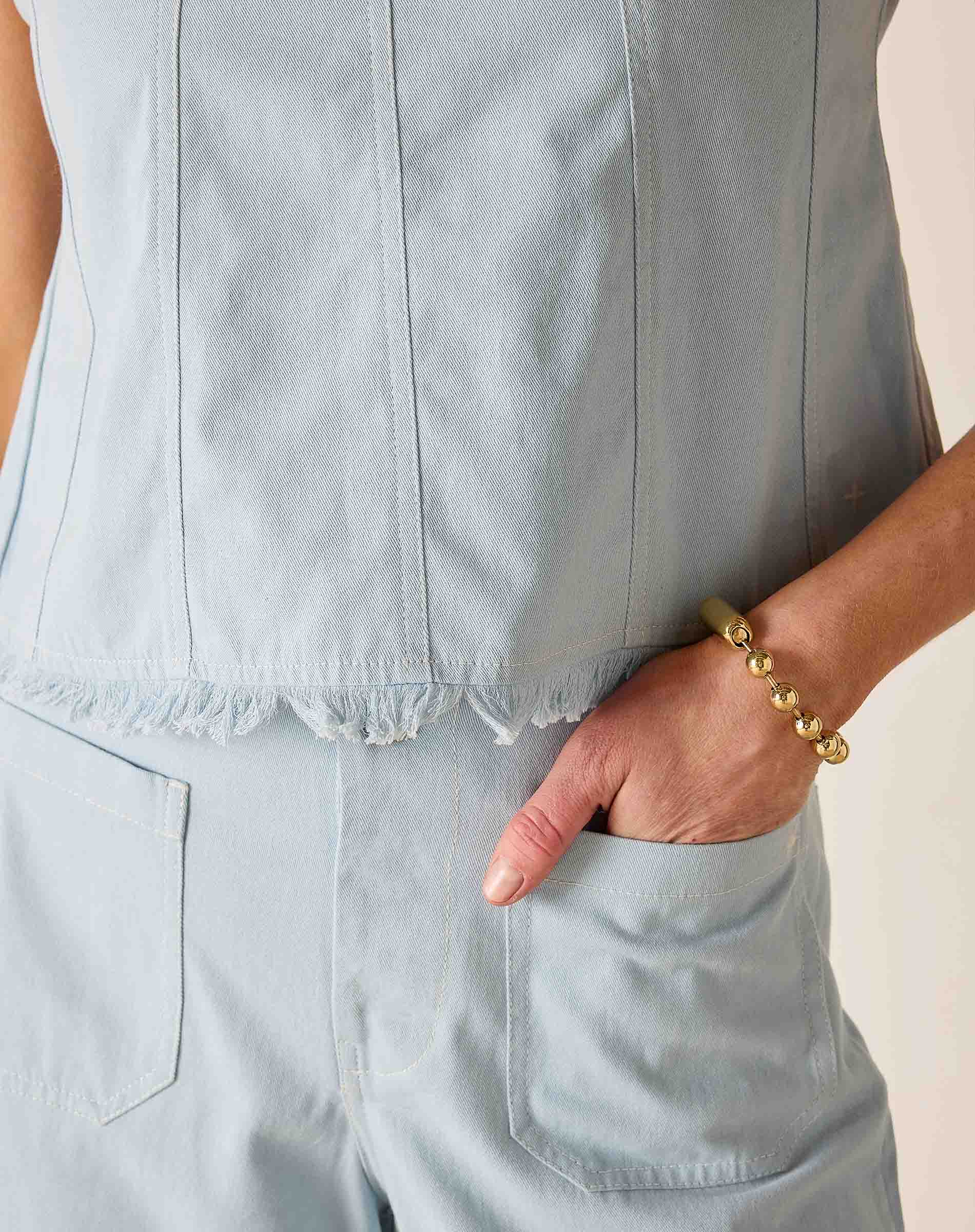 Light blue sleeveless top worn by a person with a gold bracelet on a neutral background