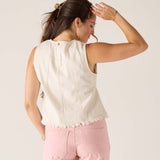 Woman wearing a white sleeveless top and pink pants against a plain background