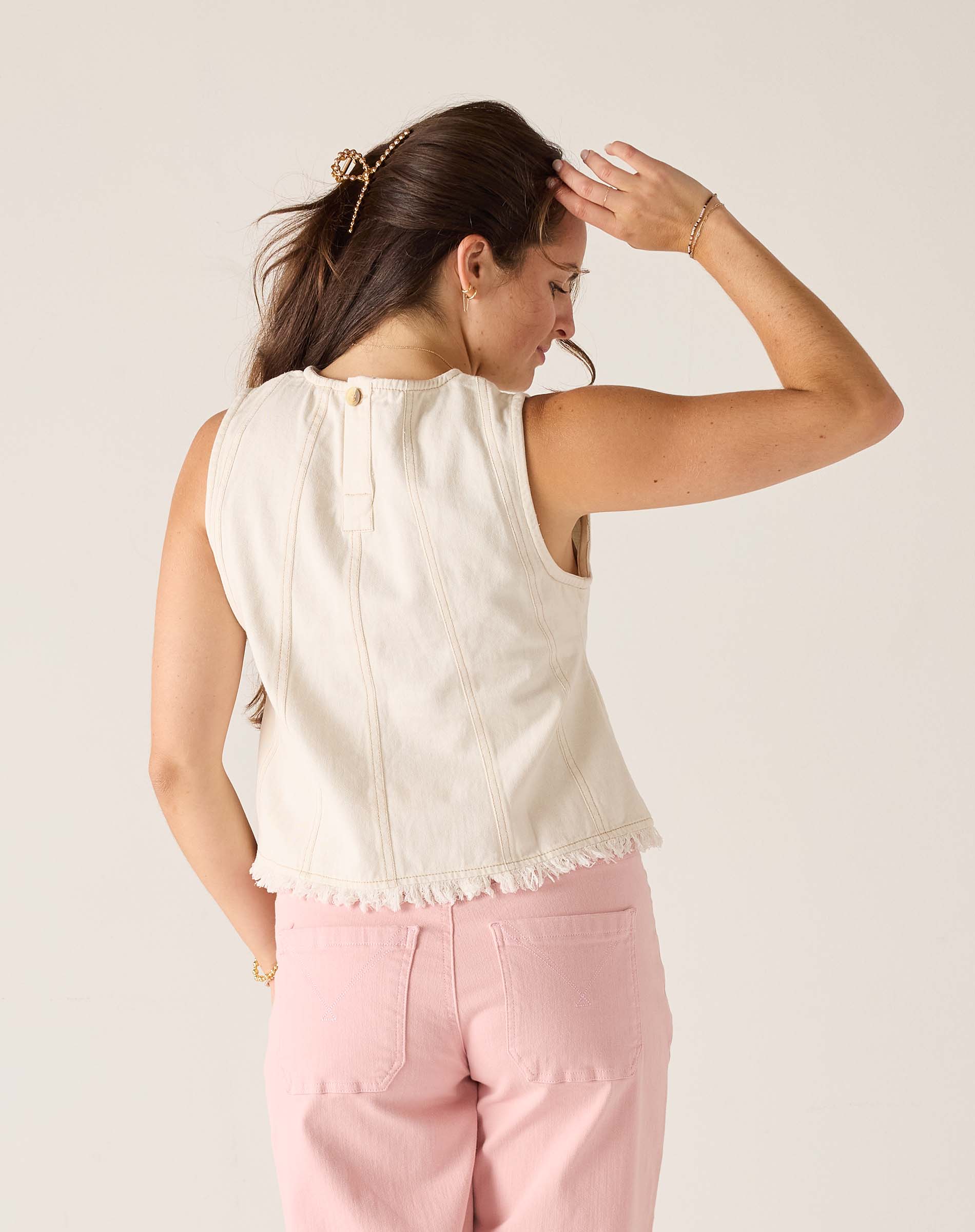 Woman wearing a white sleeveless top and pink pants against a plain background