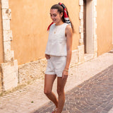 Woman walking on a cobblestone street wearing a white sleeveless top and shorts with red shoes.
