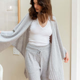 Woman wearing a gray cardigan, white top, and gray pants in a neutral setting