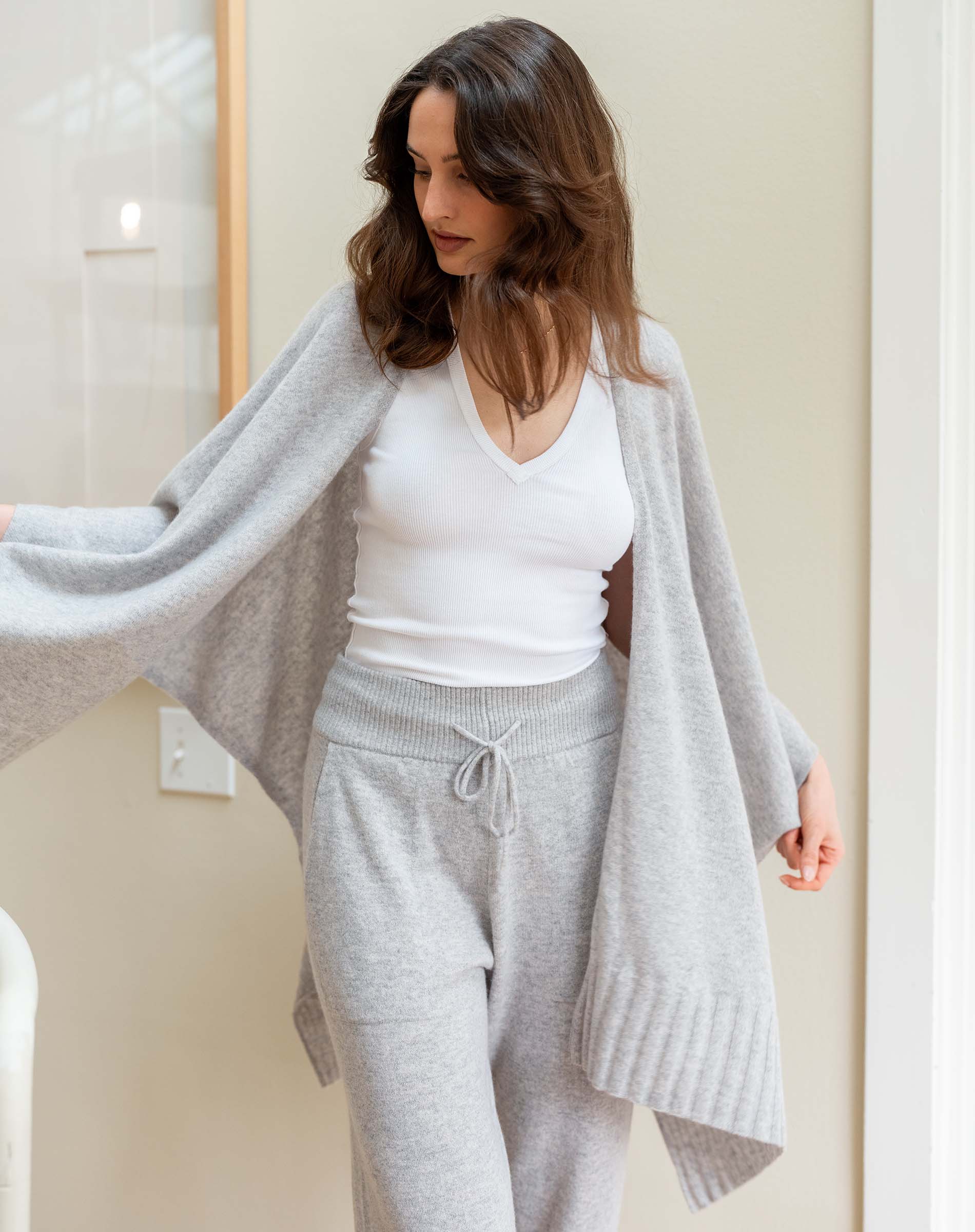 Woman wearing a gray cardigan, white top, and gray pants in a neutral setting