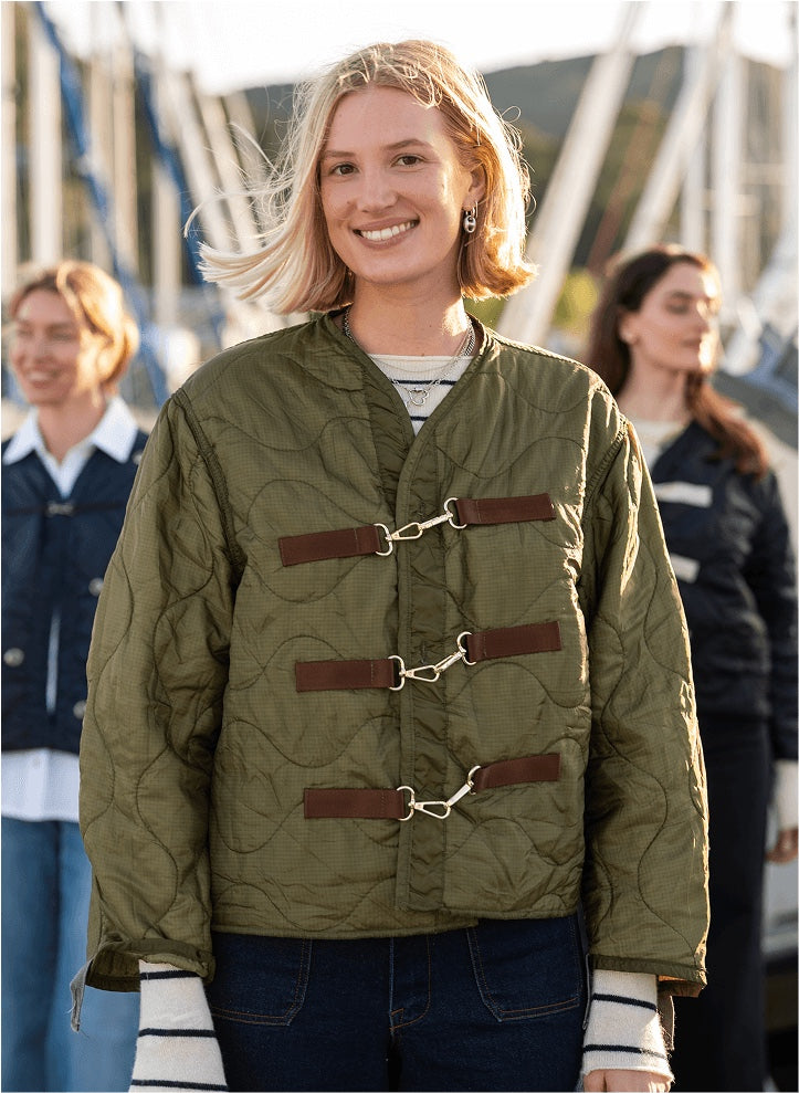 Woman wearing a green quilted jacket with brown leather straps, standing outdoors.