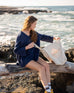 woman looking into mersea oversized canvas tote in neutral flax on a log near water
