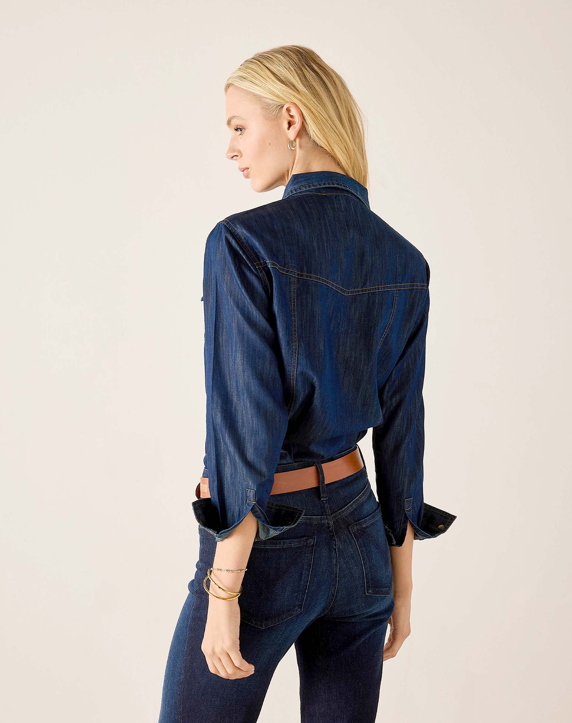 Back view of women's travel-friendly dark blue denim button-up shirt with flared cuffs and matching jeans.