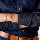 Dark wash denim button-up shirt with a leather belt and gold bracelets.