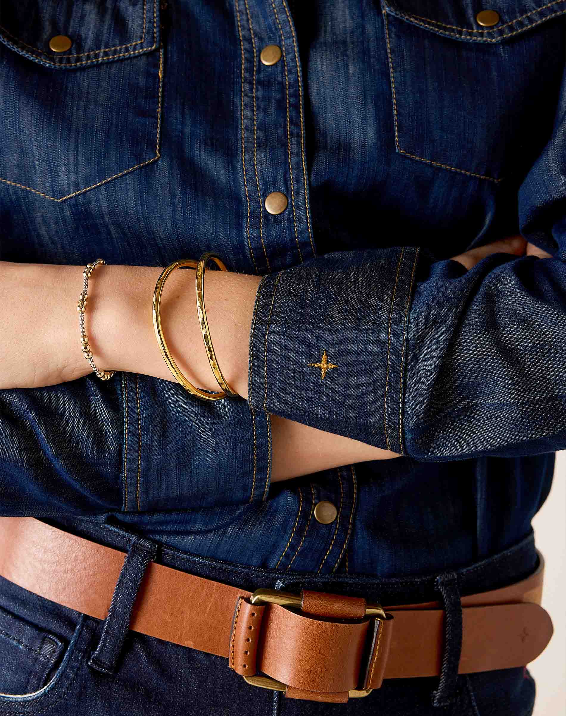 Dark wash denim button-up shirt with a leather belt and gold bracelets.