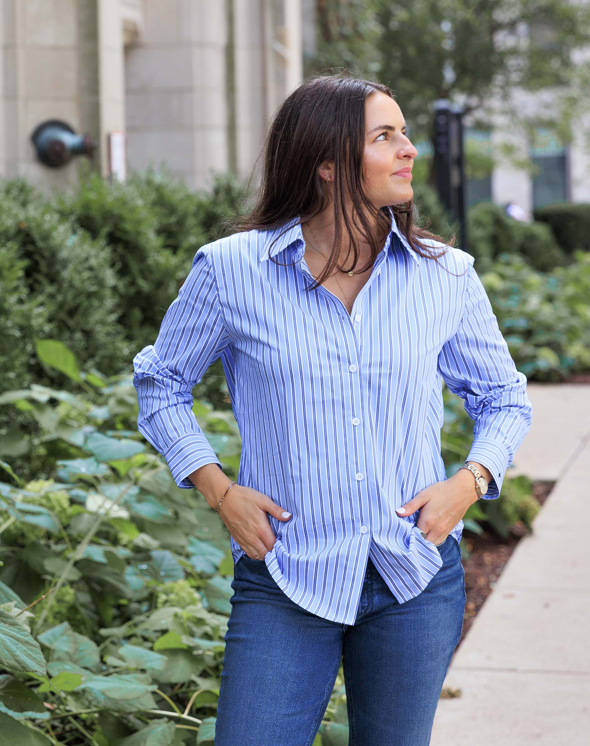 Woman wearing a blue striped shirt and jeans standing outdoors.