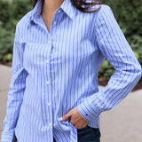 Woman wearing a blue and white striped shirt with a blurred outdoor background