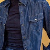 Person wearing a blue denim jacket over a dark sweater against a yellow background