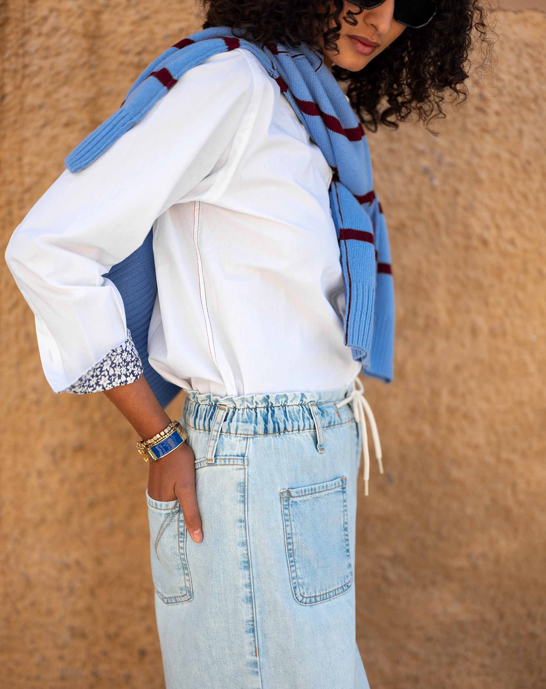 Person wearing a white shirt, blue jeans, and a blue plaid scarf against a beige background