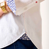 Close-up of a person wearing a white shirt with floral cuffs and a gold watch, on a plain background.