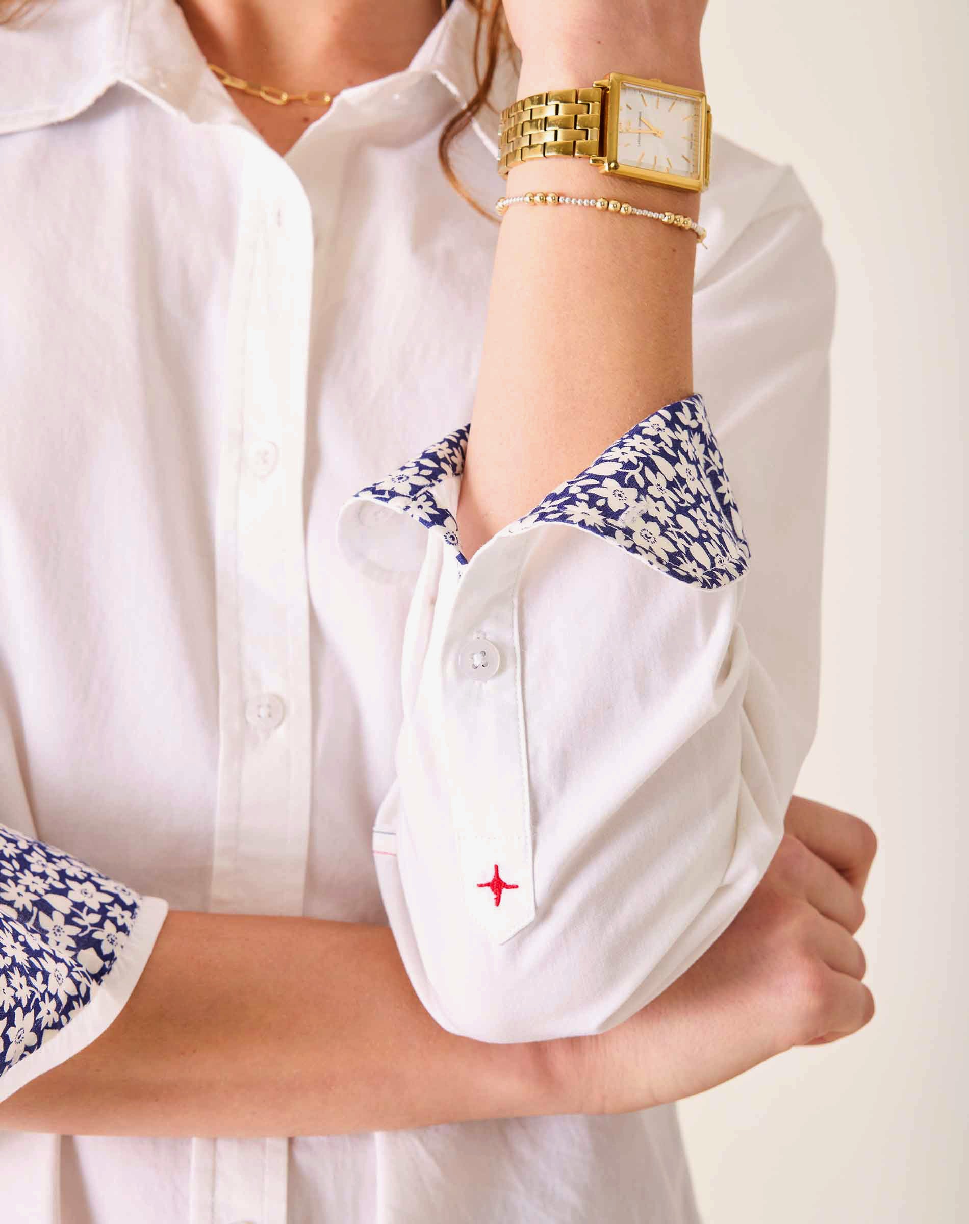 Close-up of a person wearing a white shirt with floral cuffs and a gold watch.
